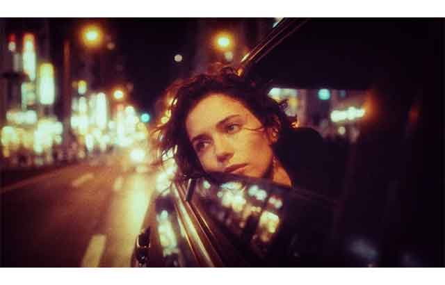 A woman leans out of a car window amid reflected city lights